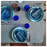 SVARTSENAP blue tablecloth with matching placemats, blue napkins, and blue cups, set on a wooden table with cutlery.