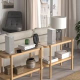 A modern living room with a SYMFONISK speaker on a wooden shelf, blending with minimalist decor, alongside a lamp and plant.