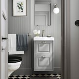Modern gray bathroom with white sink cabinet, beveled edges, wall-mounted, with black toilet, checkered floor, gray towels, and round mirror.