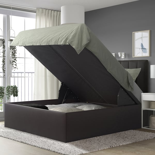 Gray upholstered ottoman bed with lift-up storage, modern bedroom, black headboard.