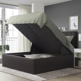 Gray upholstered ottoman bed with lift-up storage, modern bedroom, black headboard.