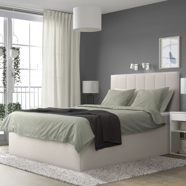 Minimalist bedroom with gray TJÅLLE bed, dark wall, plants, lamp, art.