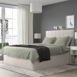 Minimalist bedroom with gray TJÅLLE bed, dark wall, plants, lamp, art.