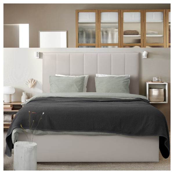 Modern minimalist bedroom with a beige upholstered headboard, gray bedding, built-in wooden shelves, and wall-mounted lights.