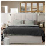 Modern minimalist bedroom with a beige upholstered headboard, gray bedding, built-in wooden shelves, and wall-mounted lights.