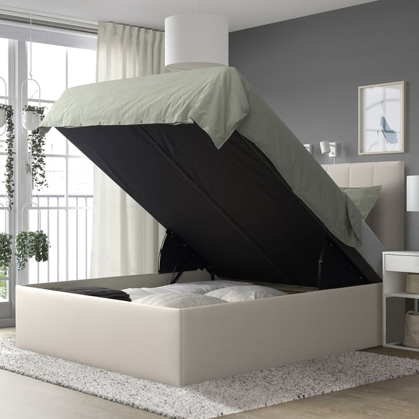 Modern TJÅLLE bed with light gray upholstery and black storage, near window.