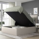 Modern TJÅLLE bed with light gray upholstery and black storage, near window.