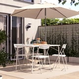 Backyard patio with beige TORPARÖ umbrella, white furniture, wooden table, and greenery.