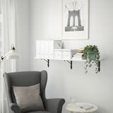 Cozy nook with TRANHULT shelf, books, plant, and armchair. Brooklyn bridge print above, minimalist decor.