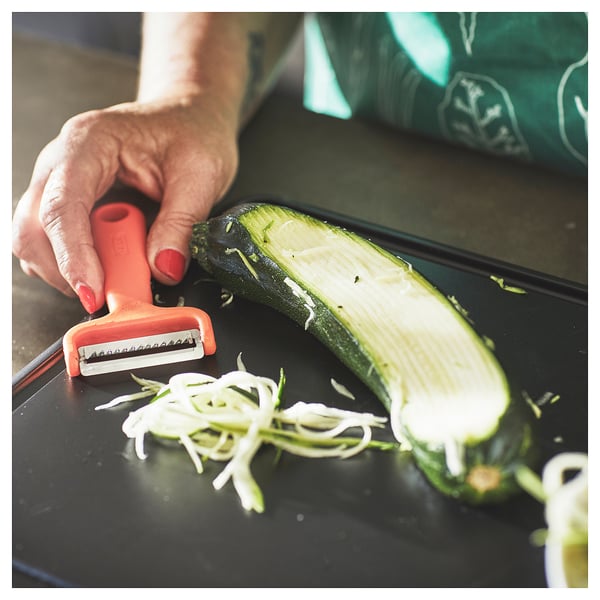 Person slicing zucchini with orange UPPFYLLD cutter on black board.