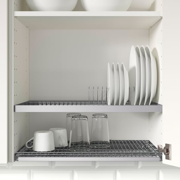 Open wall cabinet with dishes stored in a draining rack, below are glasses and mugs on a wire rack, set in a clean, white kitchen.