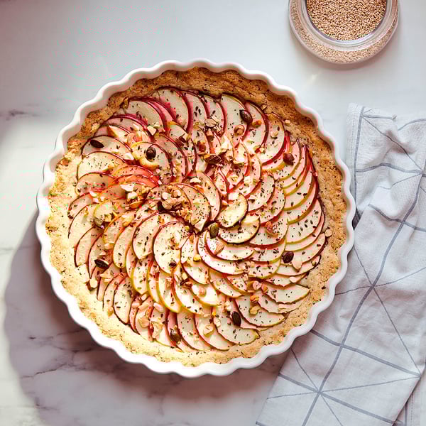 White wavy-edged pie dish with apple tart, on marble, striped cloth.