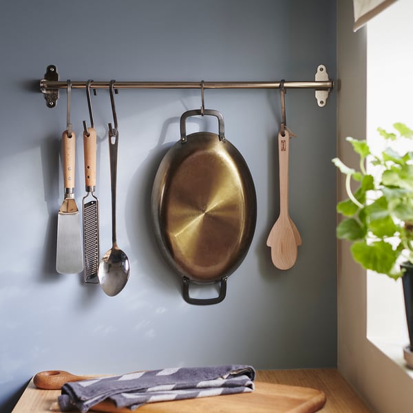 Kitchen scene with carbon steel roasting pan on hooks, wooden and metal utensils, and checkered cloth on wood.