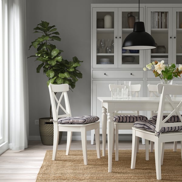 Minimalist dining room with white furniture, striped cushions, houseplant, and lamp.