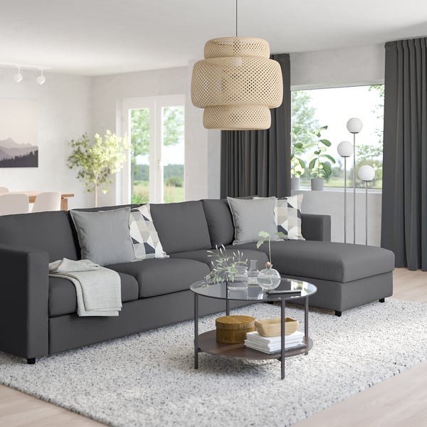 Modern grey sectional sofa with chaise, stylishly arranged living room, glass coffee table, bamboo lights, large window, dining area, floor lamp.
