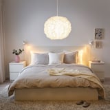 Bedroom with VINDKAST lamp over bed, beige bedding, and side tables with lamps and flowers.