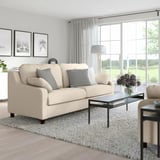 Cozy living room with beige VINLIDEN sofa, black-framed glass table, curtains, rug, and art. Sofa is large and inviting.
