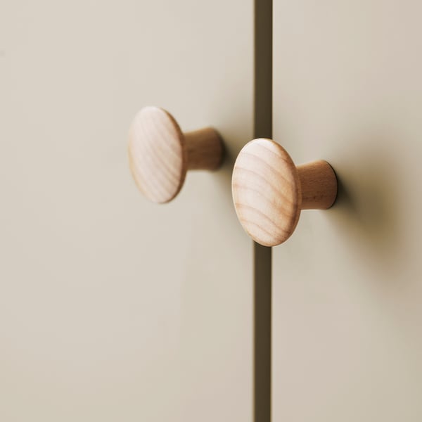 Two smooth, light-colored wooden knobs mounted on a beige cabinet, showcasing a sleek and simple design.