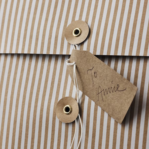 Small striped kraft paper gift bag with brass-riveted string handle tied to a to anne tag.
