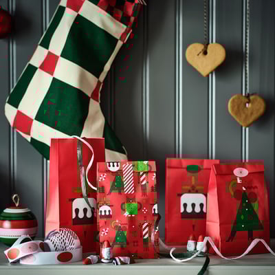 Four red paper bags, three upright with green christmas tree designs, one flat with a gingerbread man.
