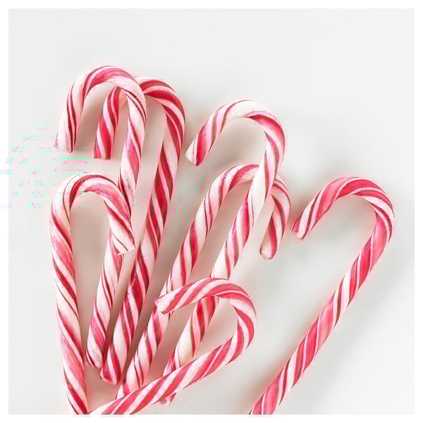 Six red and white striped candy canes, arranged casually on white surface.