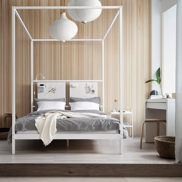 Modern bedroom with VITARNA four-poster bed, grey linens, two large lamps, plant, and dresser.