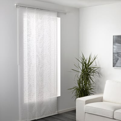 Sheer curtains covering a window, allowing light while offering privacy, with a modern plant and chair nearby.