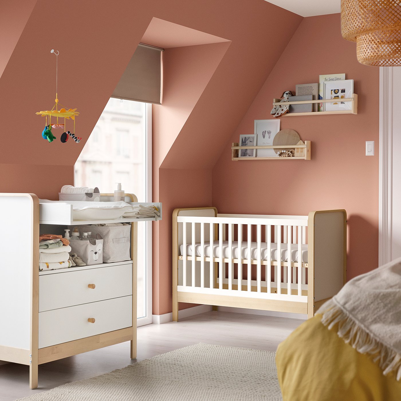 Berçário moderno com paredes cor-de-rosa, berço branco, trocador, prateleiras e móbile. Decoração suave e convidativa.