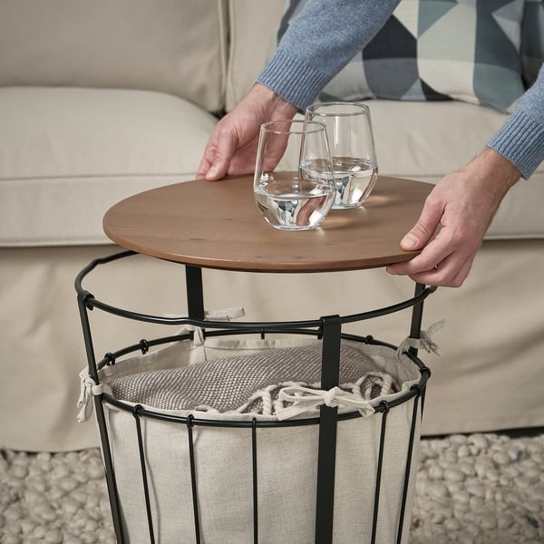 Pessoa pega copos na mesa ÄNGESBYN, demonstrando a sua utilização como café ou mesa de apoio com arrumação.