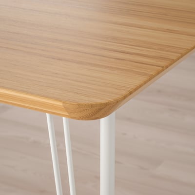 Close-up da borda da mesa moderna, tampo de bambu liso sobre pernas de metal branco.