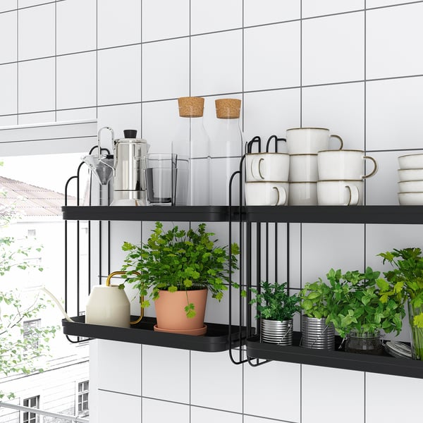 As modernas prateleiras de parede de metal preto contêm canecas brancas, potes de vidro e plantas verdes em uma sala de azulejos brancos, misturando estilo com elementos naturais.