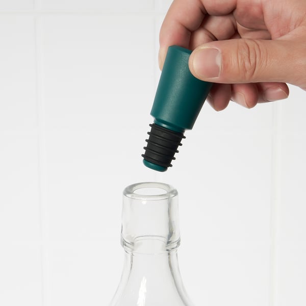 Pessoa colocando rolha de garrafa azul-petróleo em gargalo transparente.