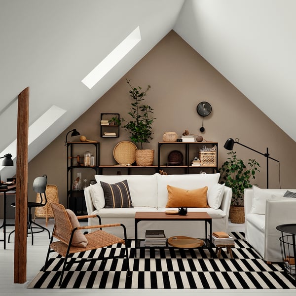 Sala de estar moderna com sofá BACKSÄLEN, candeeiro, tapete, cadeiras de vime e estante encostada à parede castanha.