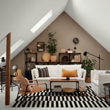 Sala de estar moderna com sofá BACKSÄLEN, candeeiro, tapete, cadeiras de vime e estante encostada à parede castanha.