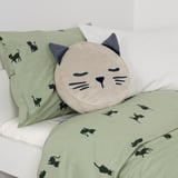 Almofada em forma de gato com bolso nas costas, para guardar itens. Parte do conjunto de roupa de cama verde com estampas de gato preto.