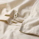 Close-up de edredom bege listrado & branco com botão, mostrando sua textura de algodão macio e design vintage.