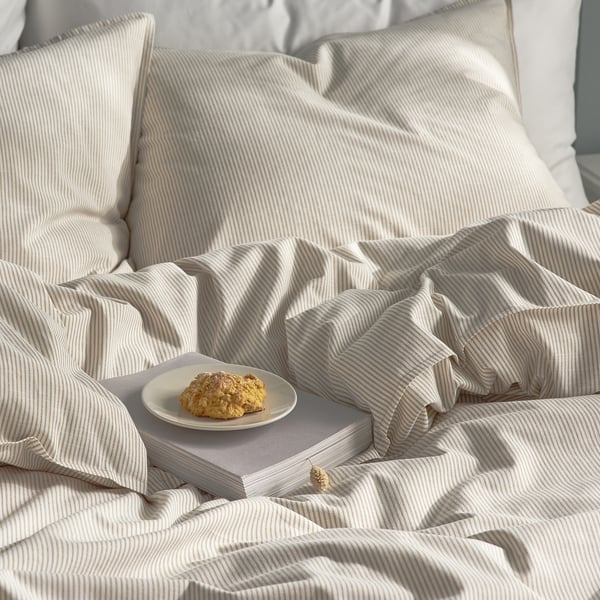 Quarto aconchegante com roupa de cama listrada. A pastelaria nos livros sugere um ambiente descontraído.