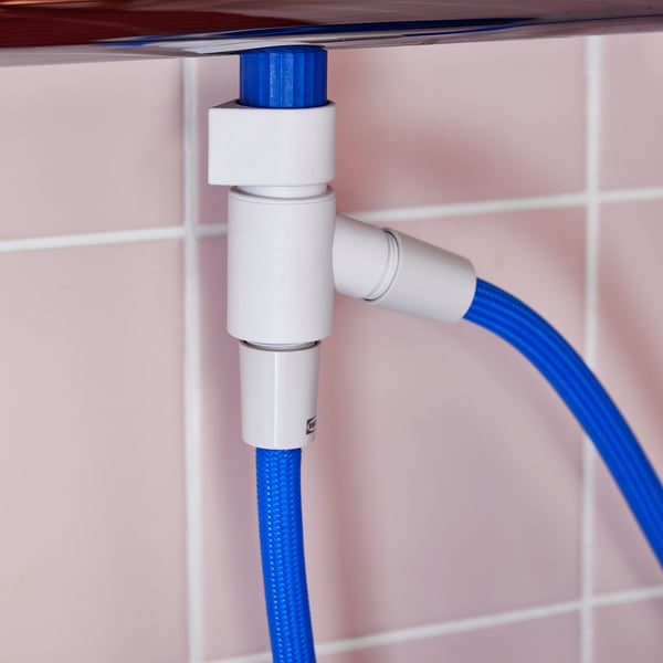 Mangueira de chuveiro azul conectada a um desviador branco montado em ladrilhos rosa claro.