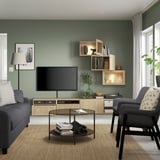 Sala de estar moderna com sofá cinza, TV em suporte de madeira, mesa de centro de vidro e cadeira cinza contra parede verde.
