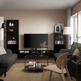 Sala de estar moderna com móvel de TV BESTÅ, sofá cinza, cadeira, tapete e mesa. TV ladeada por prateleiras com livros e decoração.