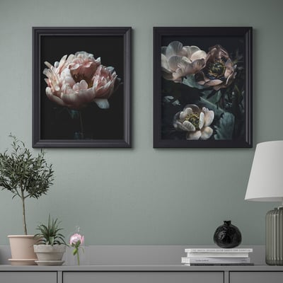Duas impressões de arte floral emolduradas estão penduradas acima de uma mesa de console exibindo uma lâmpada, vaso e planta.