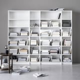 Grandes estantes brancas BILLY com inúmeros livros e decoração minimalista. Design limpo, organizado e moderno.