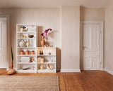 Sala de estar neutra com estantes brancas BILLY, paredes bege, piso de madeira e vários itens decorativos.