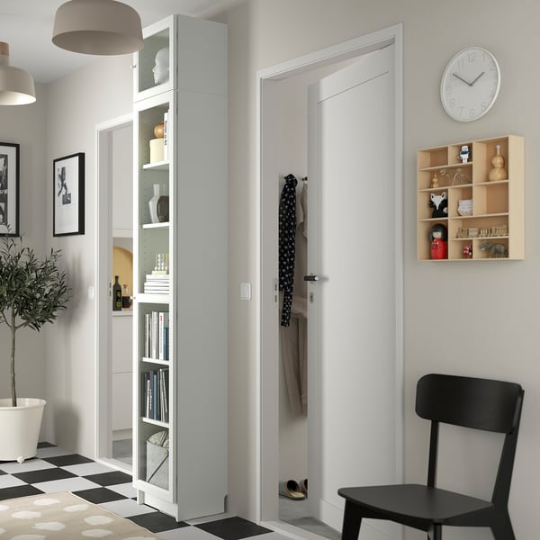 Entrada minimalista com estante branca BILLY, cadeira preta, relógio e casacos pendurados.