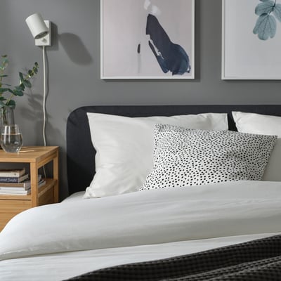 Almofada BJÖRKGRÅMAL pontilhada em preto e branco por hanna wilcox na cama, ecológica e minimalista.