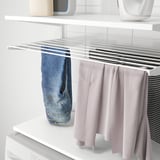 Armazenamento de parede BOAXEL: estendal comporta jeans, calças rosa e camisa listrada. Fácil organização da lavanderia.