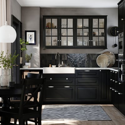 Cozinha preta moderna com armários de vidro, pia preta e tapete listrado. Design elegante com madeira escura e backsplash metálico.