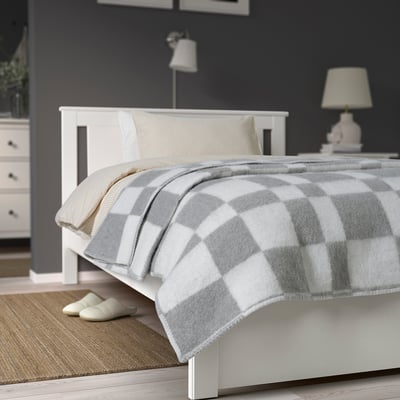 Colcha branca BORSTTÅG c/ padrão cinza em cama grande encostada à parede escura.