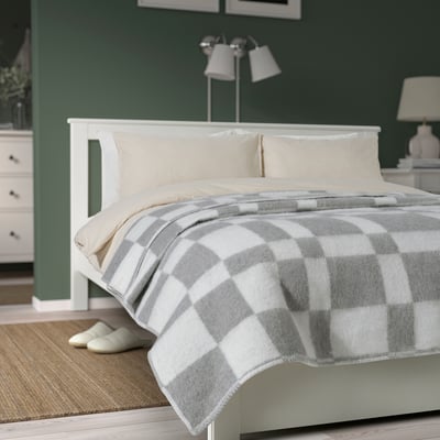 Colcha BORSTTÅG xadrez cinzenta em cama grande, encostada à parede verde.