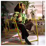 Pessoa em cadeira BRÄNNBOLL, ouvindo música com fones de ouvido. A malha permite o fluxo de ar e se ajusta para balançar e inclinar para maior conforto.